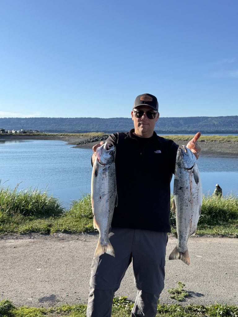 Philip Licht holding two freshly caught salmon beside an Alaska river